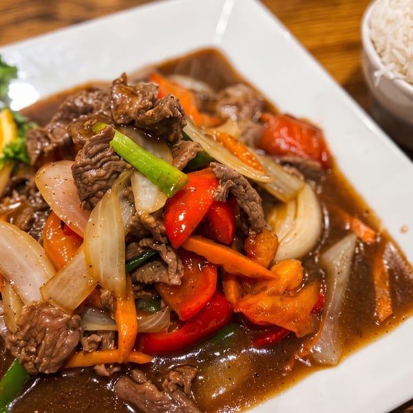 Stir-fried beef with colorful vegetables and a side of white rice on a wooden table.