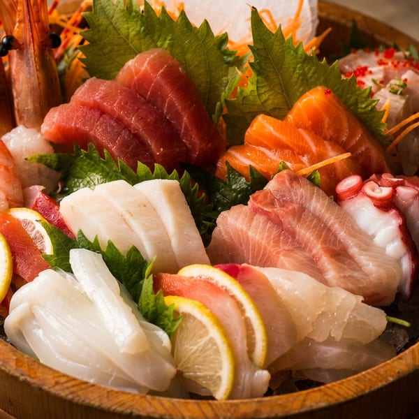 A large wooden bowl filled with various sashimi, including tuna, salmon, octopus, squid, and shrimp.
