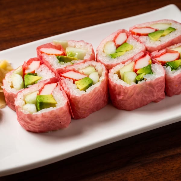 Pink sushi rolls with crab, avocado, and cucumber, served with wasabi and ginger on a white plate.
